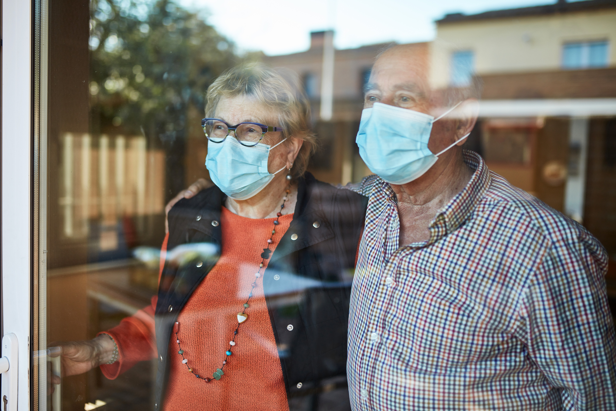 Worried senior couple looking through window at home in quarantine