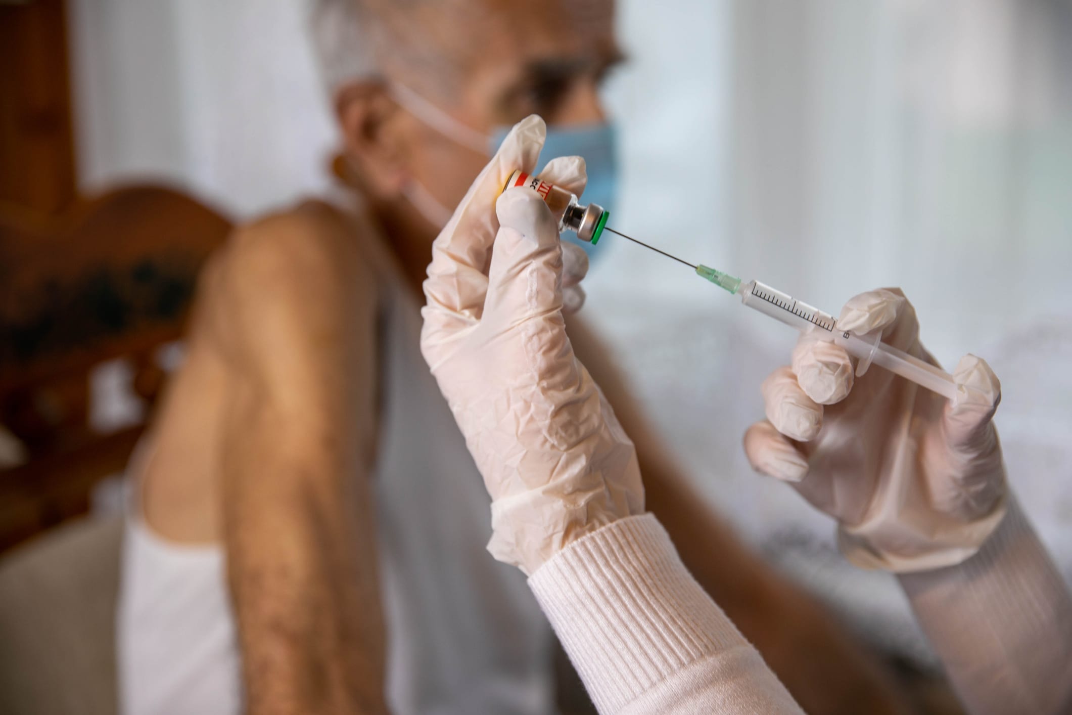 Senior man getting vaccinated by visiting nurse at home