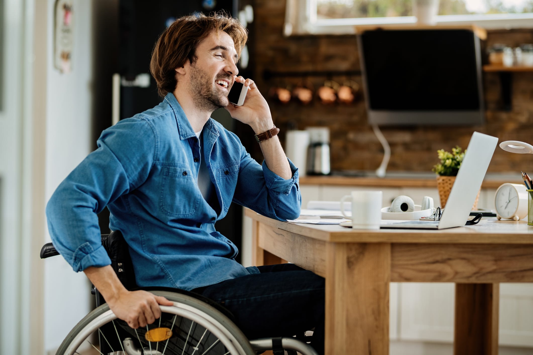 Happy freelancer in wheelchair communicating over mobile phone while working at home.
